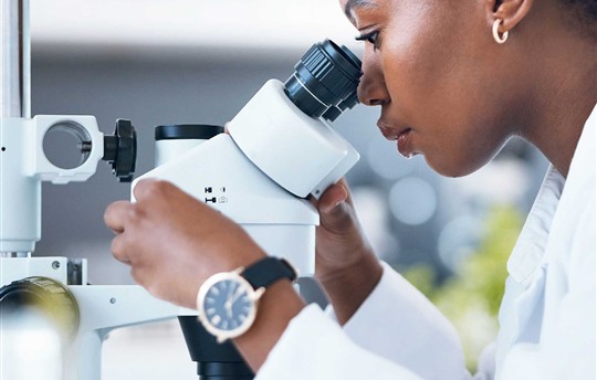 young black woman looking into a microscope in a lab