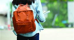 Back of student girl holding books and carry school bag while walking in school campus background