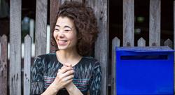 smiling woman standing near the fence with a blue mailbox