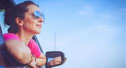 Woman in pink shirt and sunglasses, leaning out car window and smiling with blue sky in the background