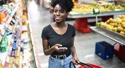 Young woman using mobile phone and choosing product in supermarket