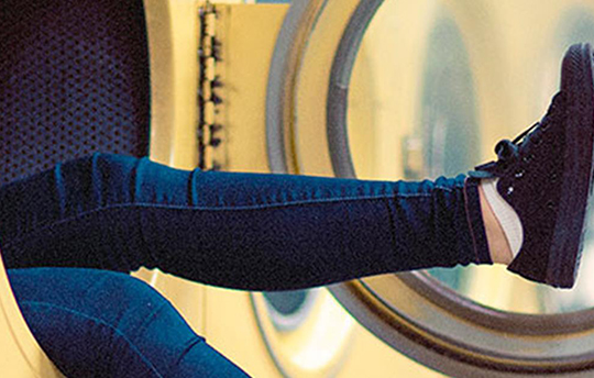 legs sticking out of a yellow clothes dryer at a laundromat