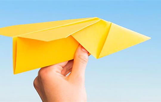 a hand holding a bright yellow paper airplane
